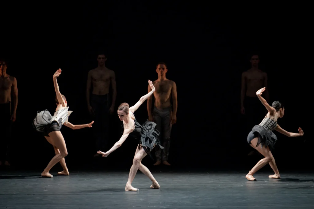 Three dancers perform in black costumes on a dark stage during Come Un Respiro